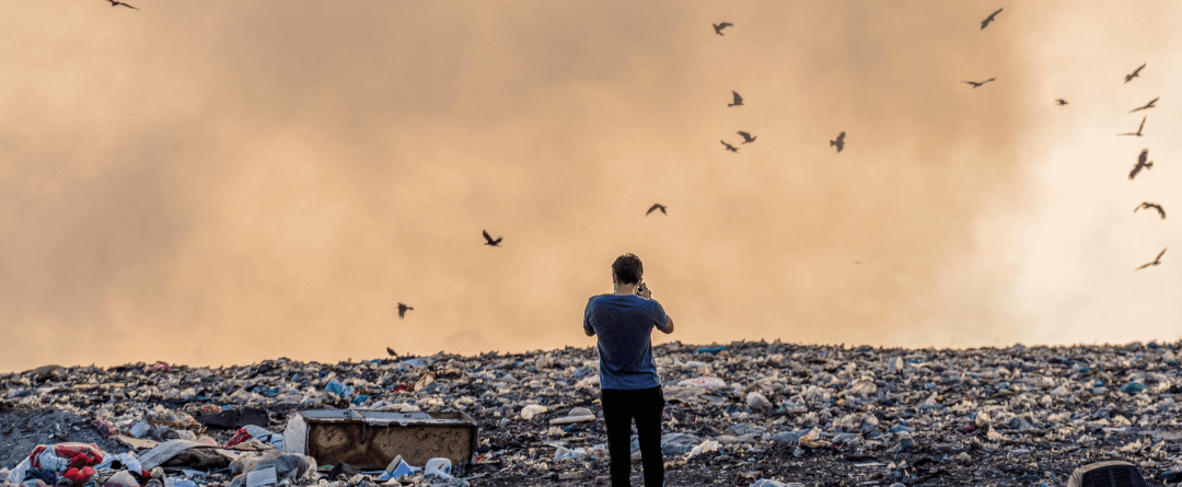 ένας άνθρωπος ανάμεσα σε σκουπίδα και πλαστικά μαύρα πουλιά πετάνε και φαίνεται η μόλυνση του περιβάλλοντος και η κλιματική αλλαγή